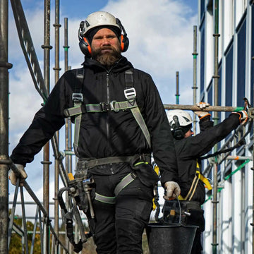 Black construction worker wearing a white hard hat with orange ear protection and a black safety harness.